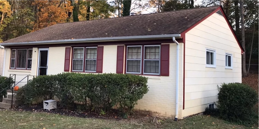 White brick ranch home with burgundy trim and shutters surrounded by shrubs
