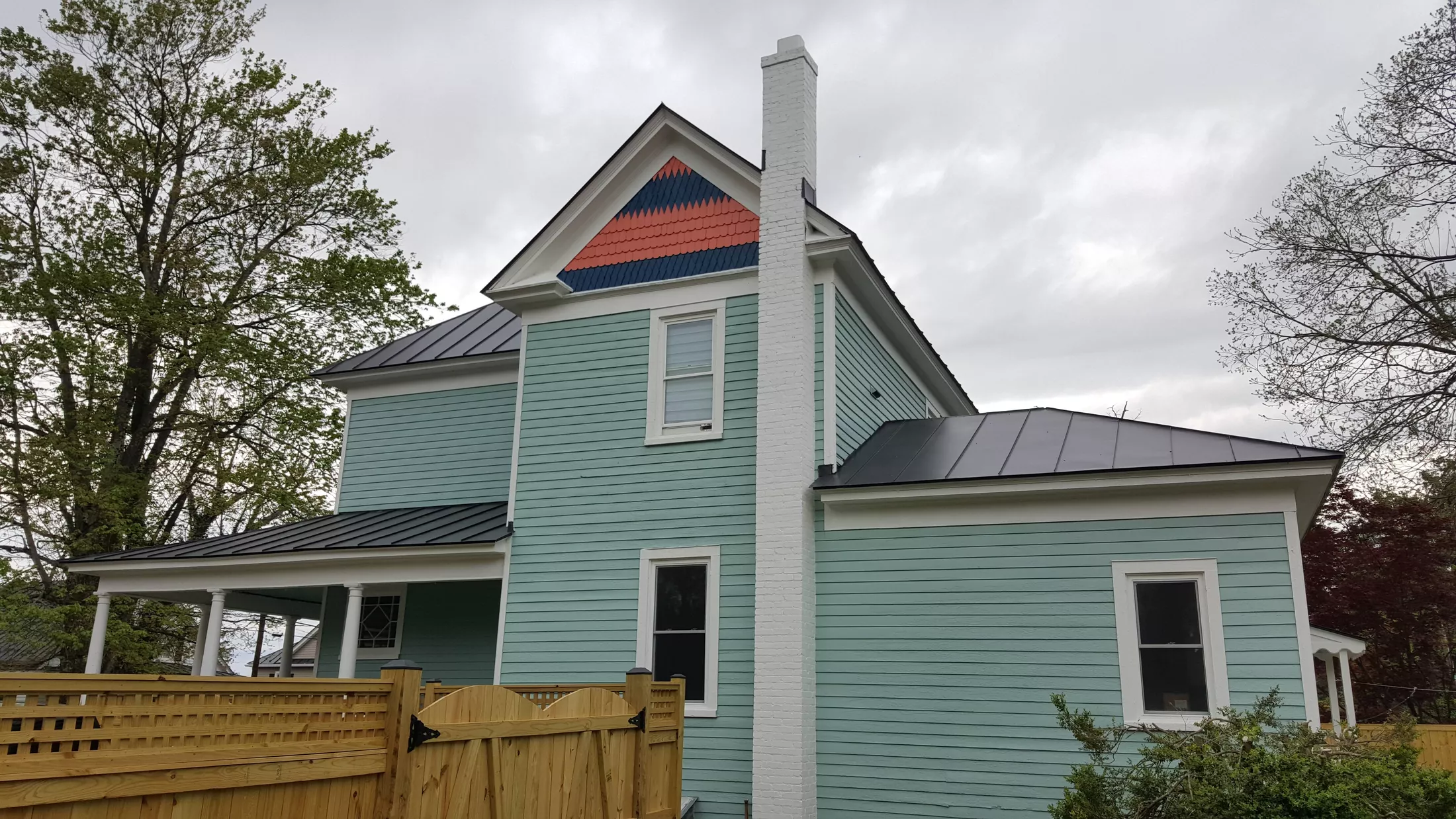 Renovated farmhouse with light blue siding, white trim, and distinctive red and blue roof pattern
