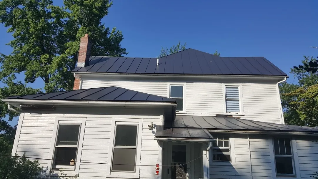 White farmhouse with black metal roof and brick chimney