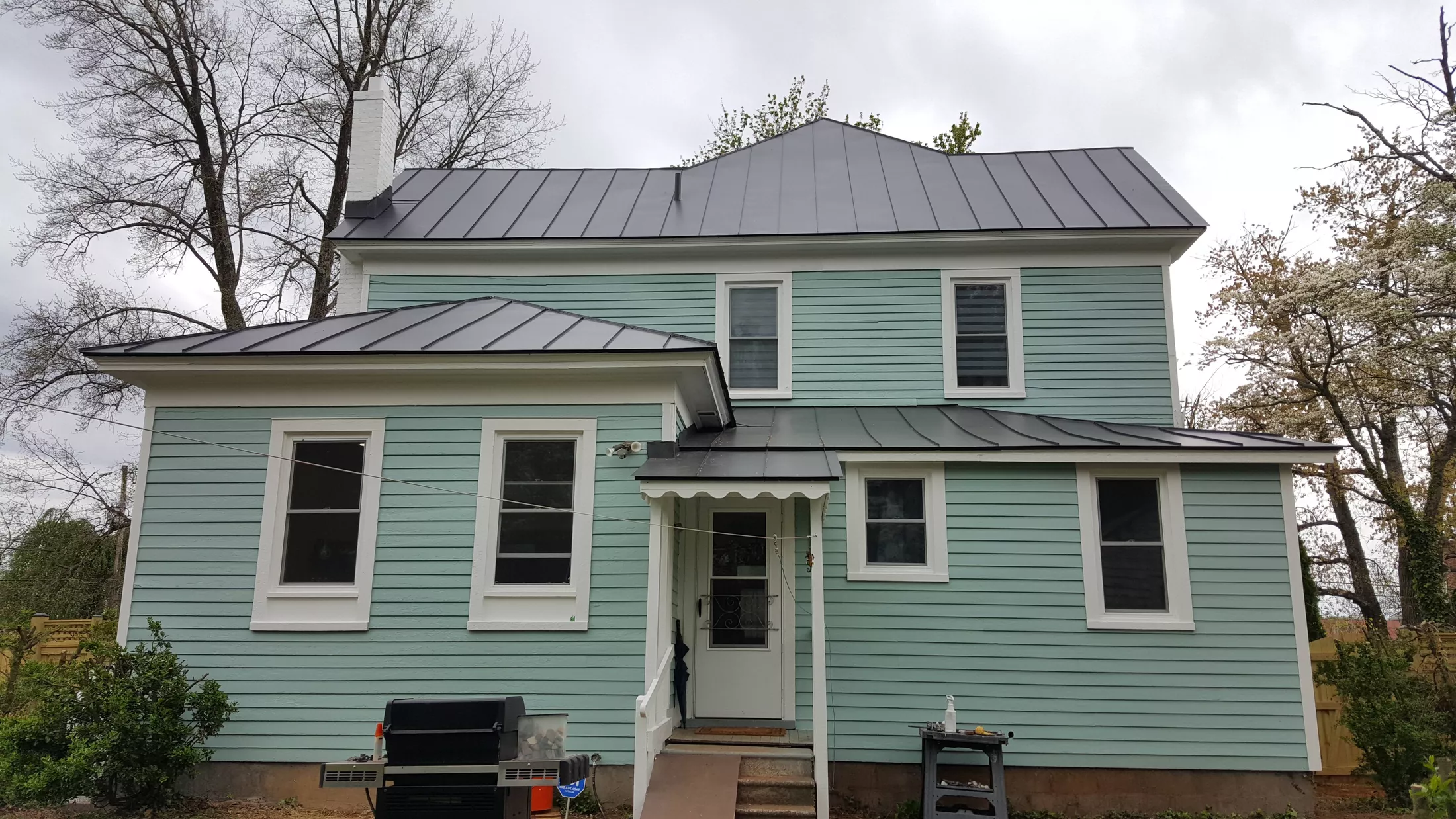 Light blue two-story house with metal roof and white trim windows