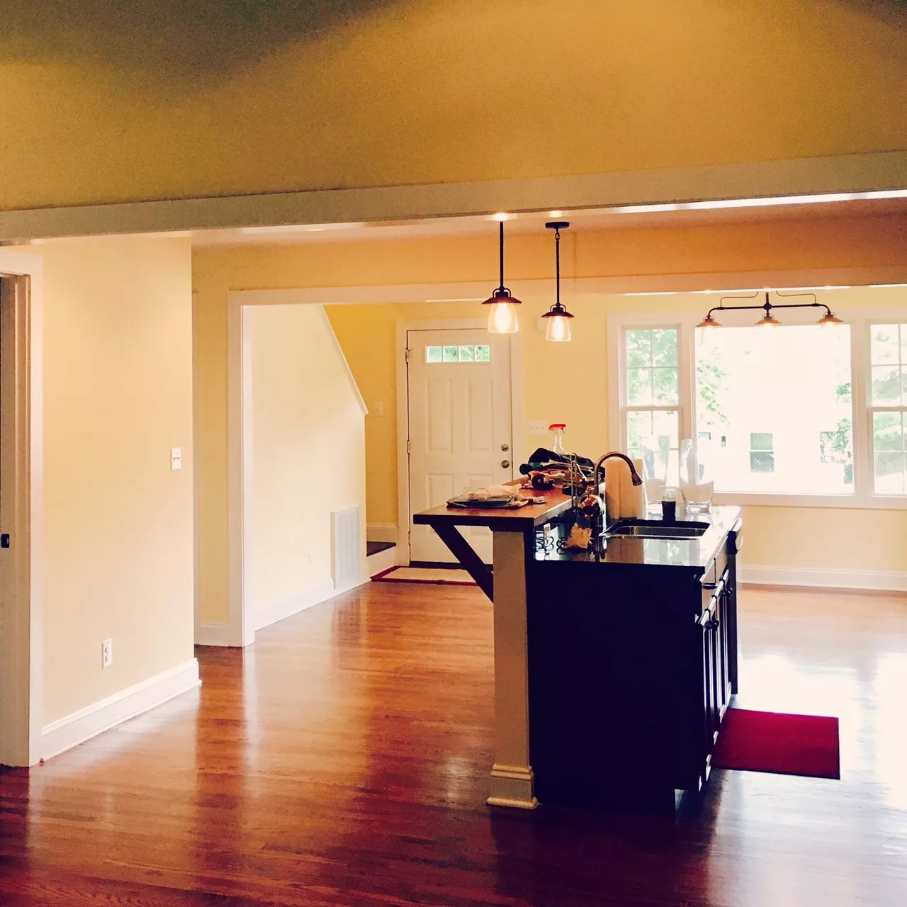 Spacious open-concept home interior with yellow walls, hardwood flooring, black kitchen island, and natural light from large windows