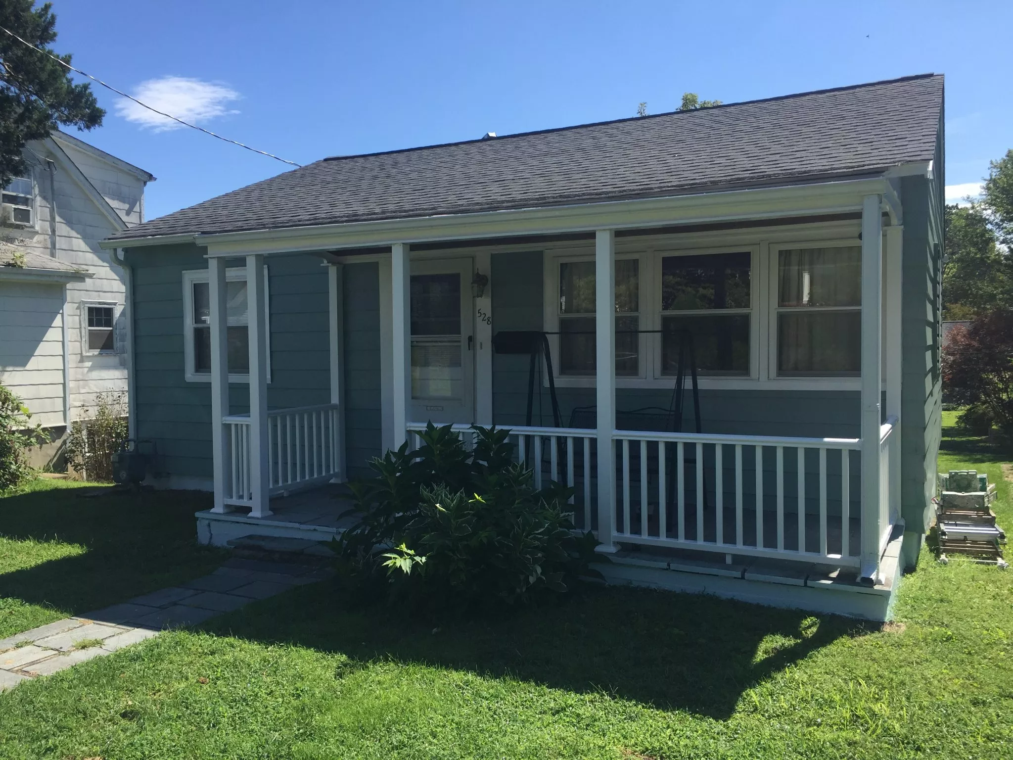 Teal cottage with white trim, screened porch, and gray roof on sunny day