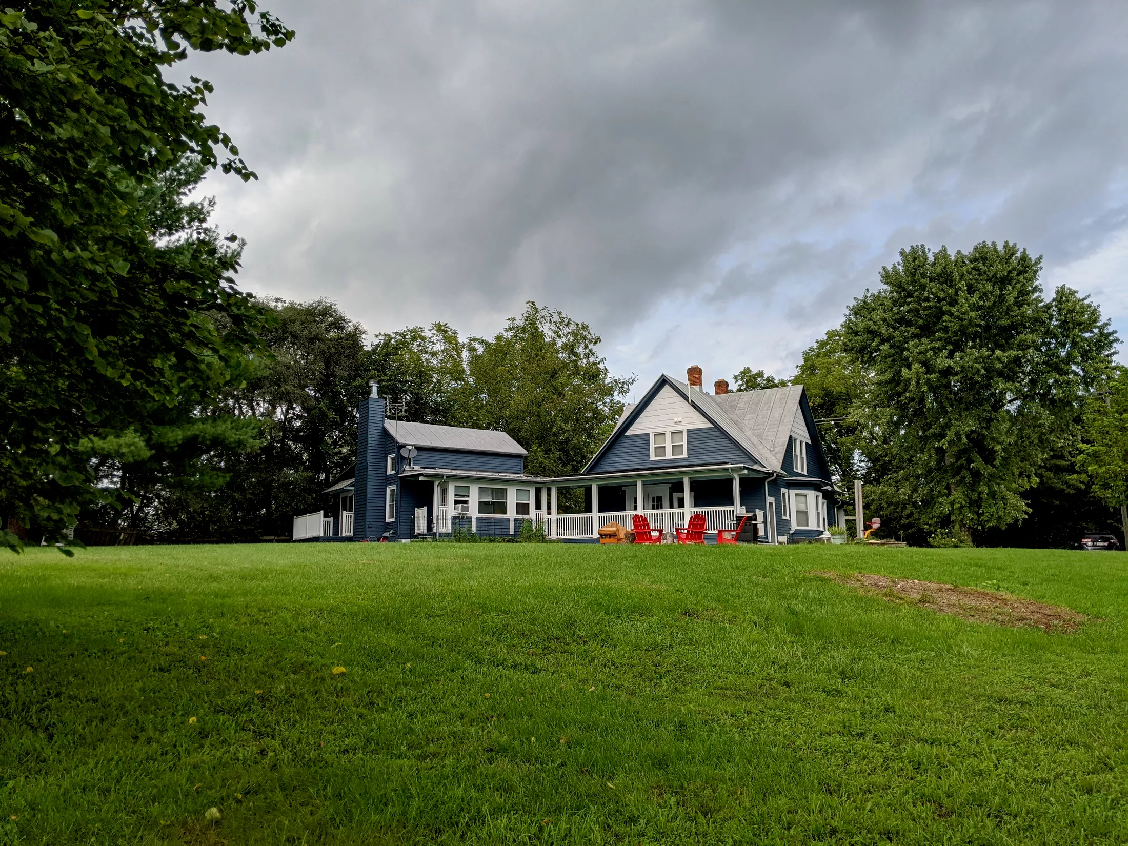 Classic farmhouse with white porch and red Adirondack chairs on expansive green lawn