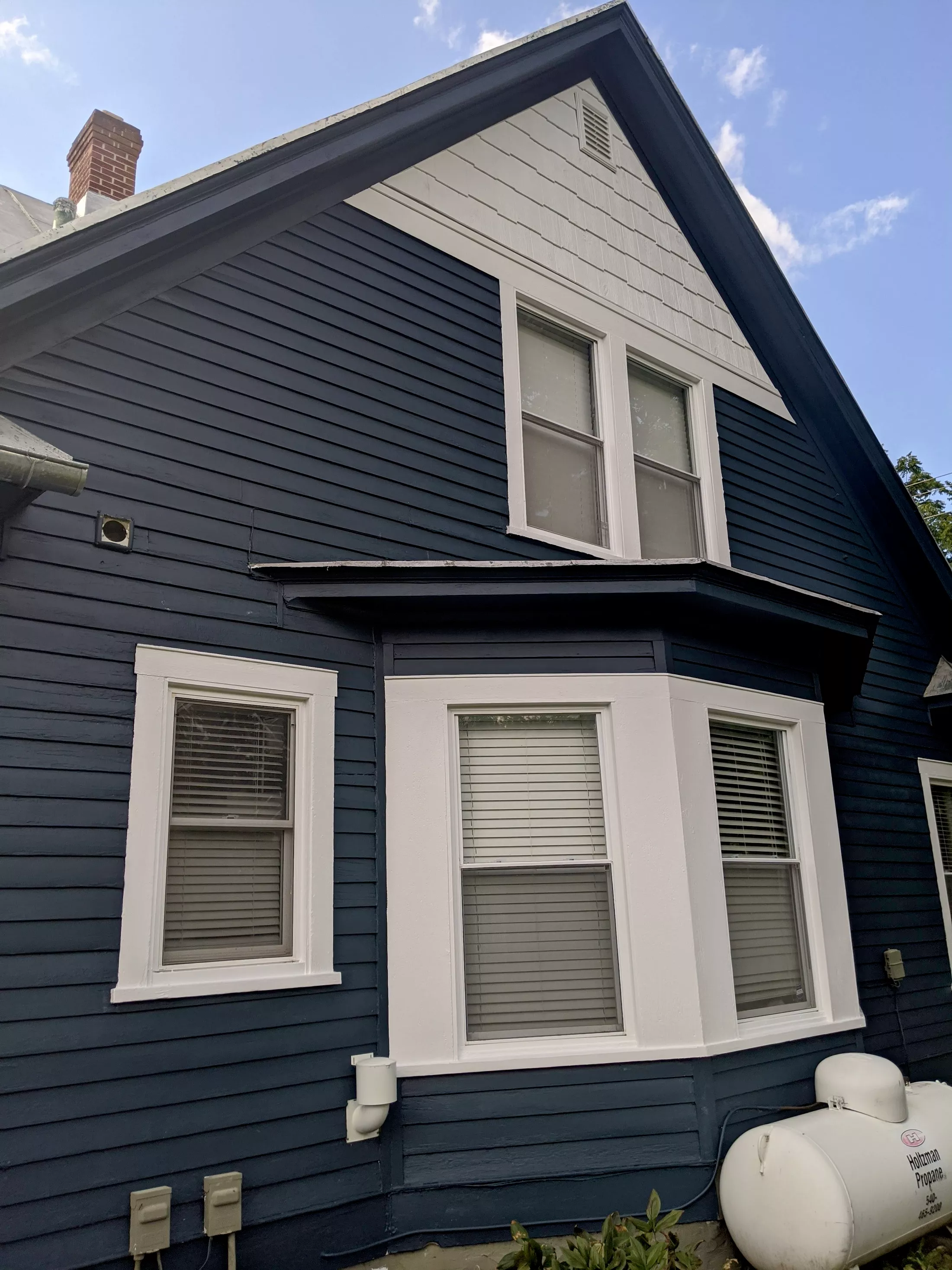 Dark blue house with white-trimmed windows and gabled roof on sunny day