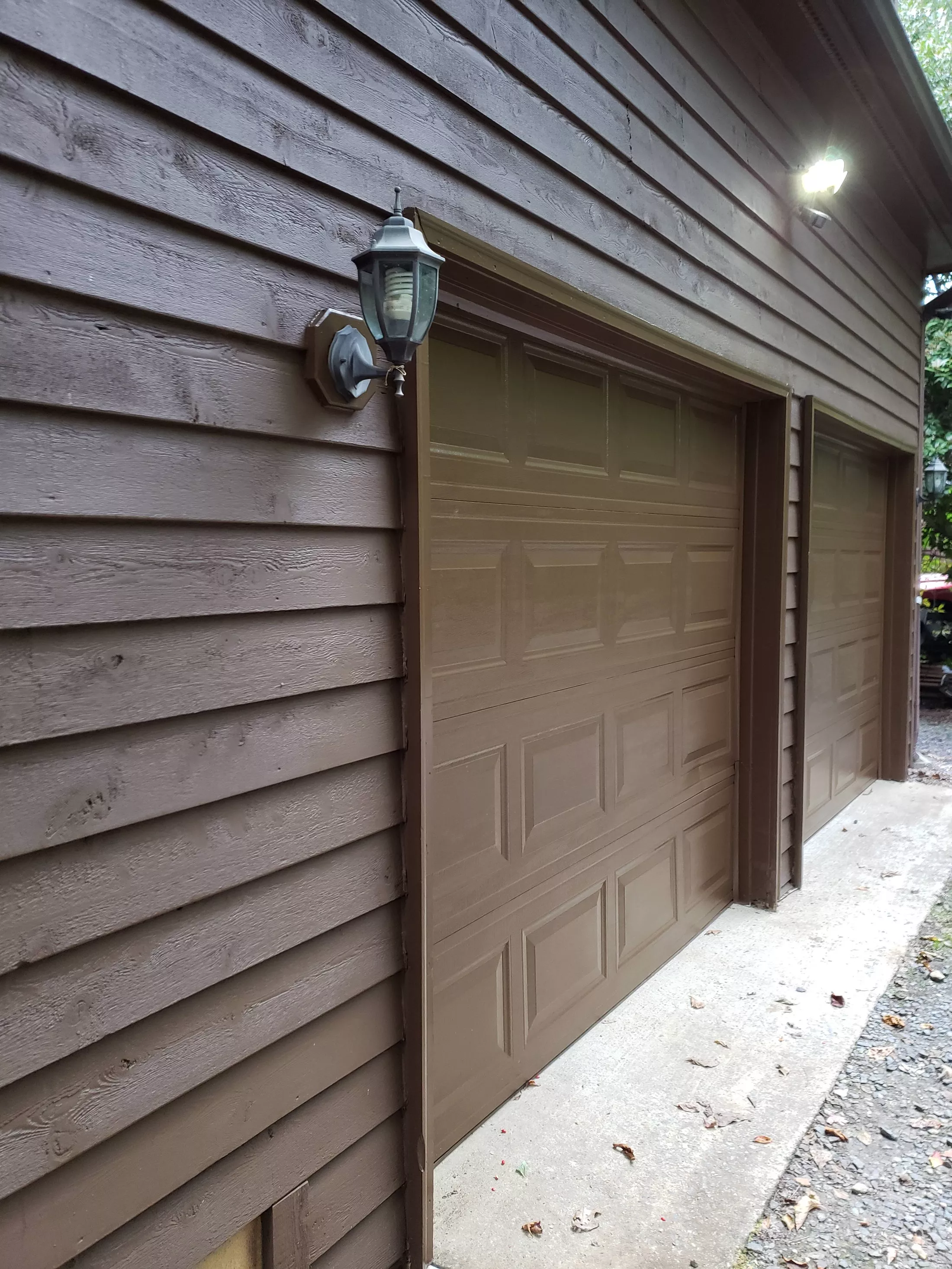 Two brown garage doors on wood-sided house with wall sconce light