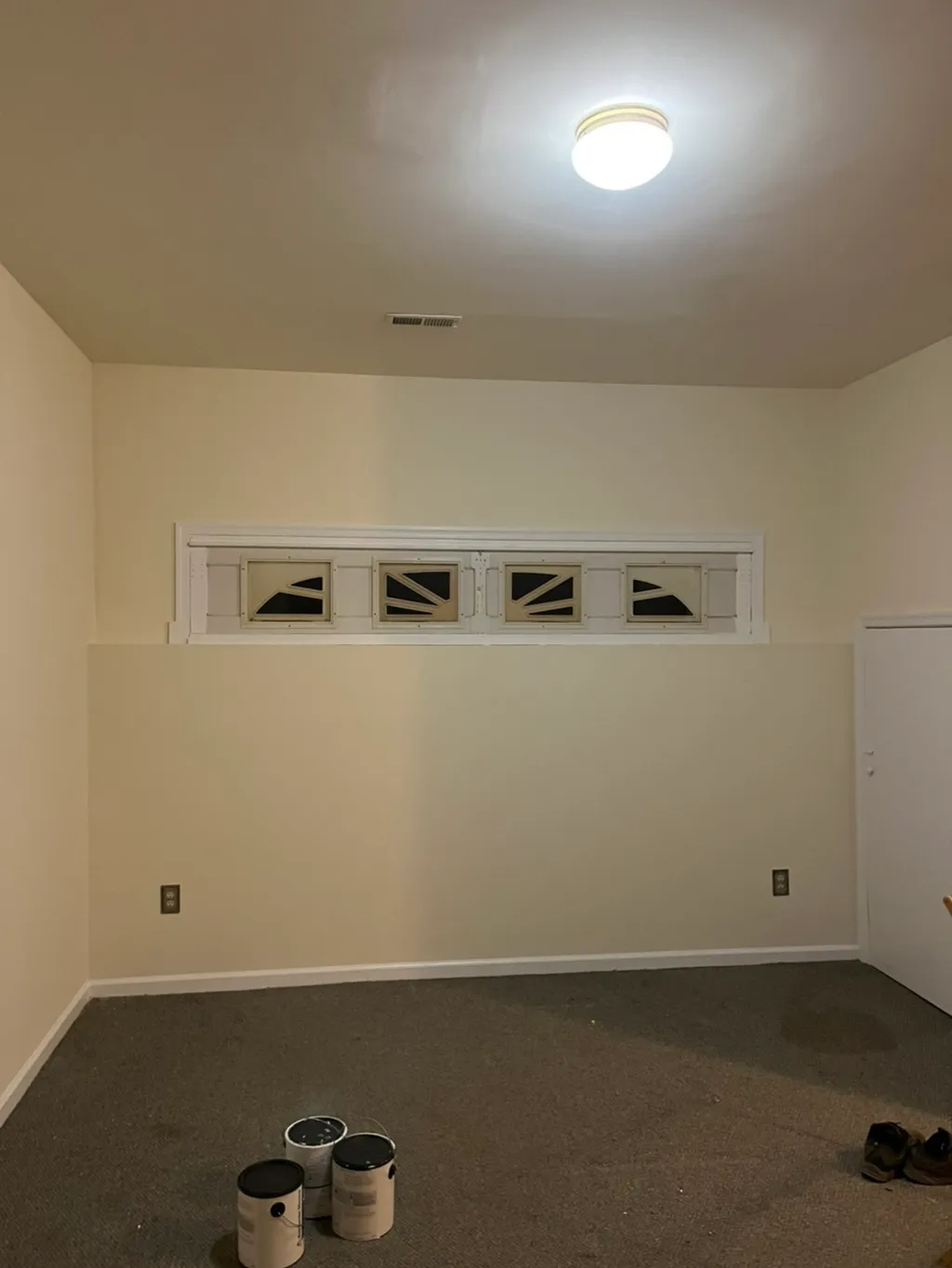 Empty room with cream walls, ceiling light fixture, and four-pane transom window with dark glass