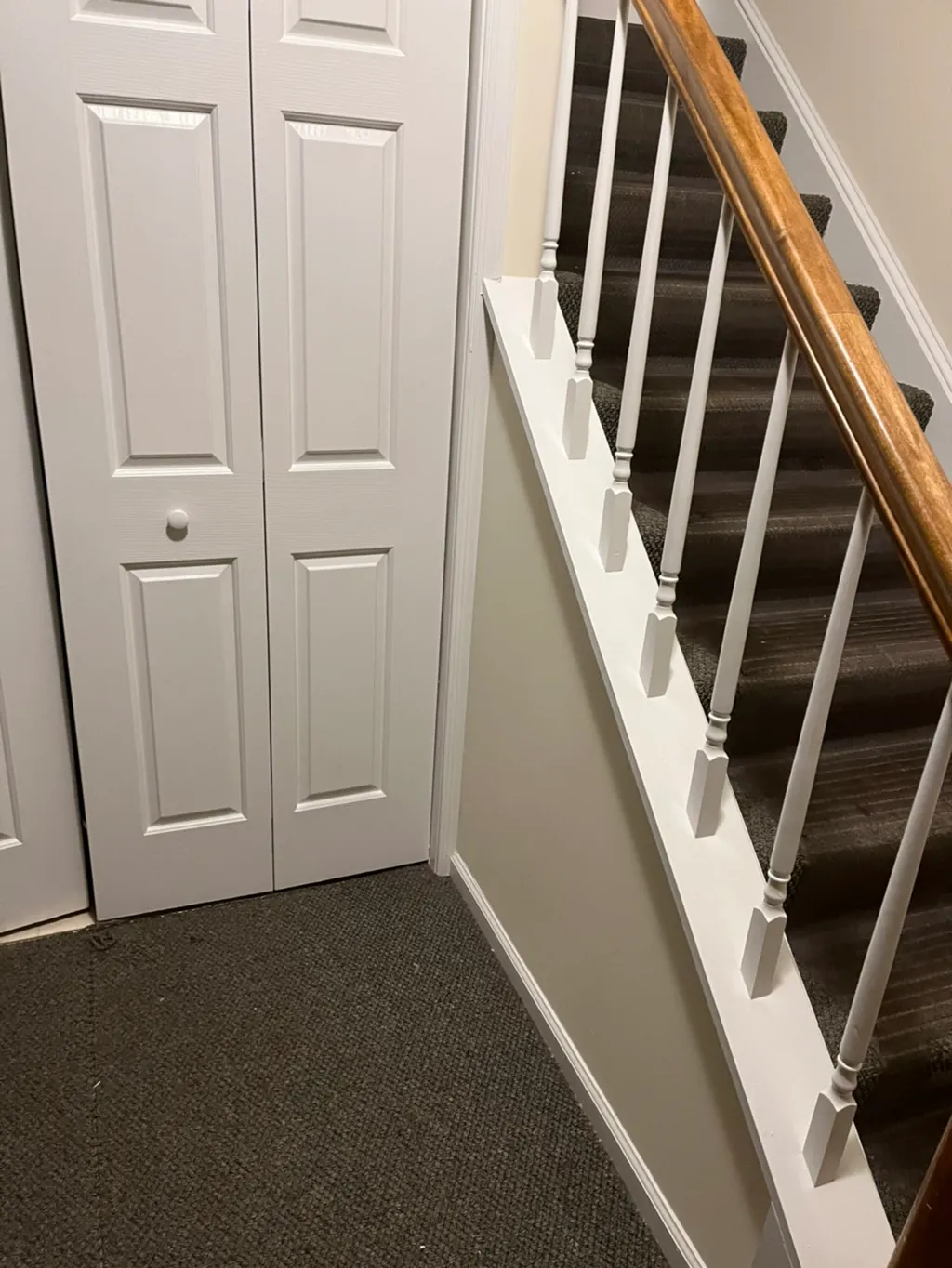 Hallway with white six-panel closet doors and wooden stair railing with dark carpeted steps