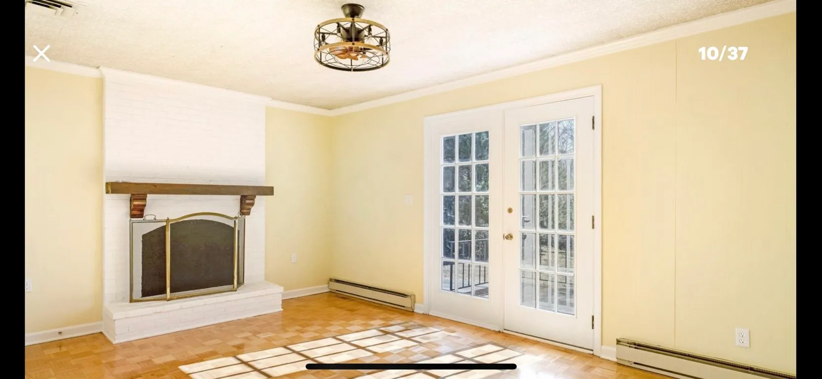 Spacious living room with fireplace, yellow walls, French doors, hardwood floor and ceiling fixture