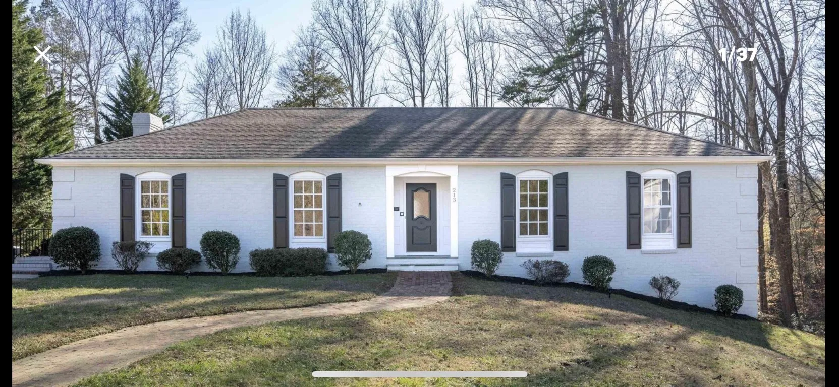 White ranch home with dark shutters, brick walkway, and manicured landscaping