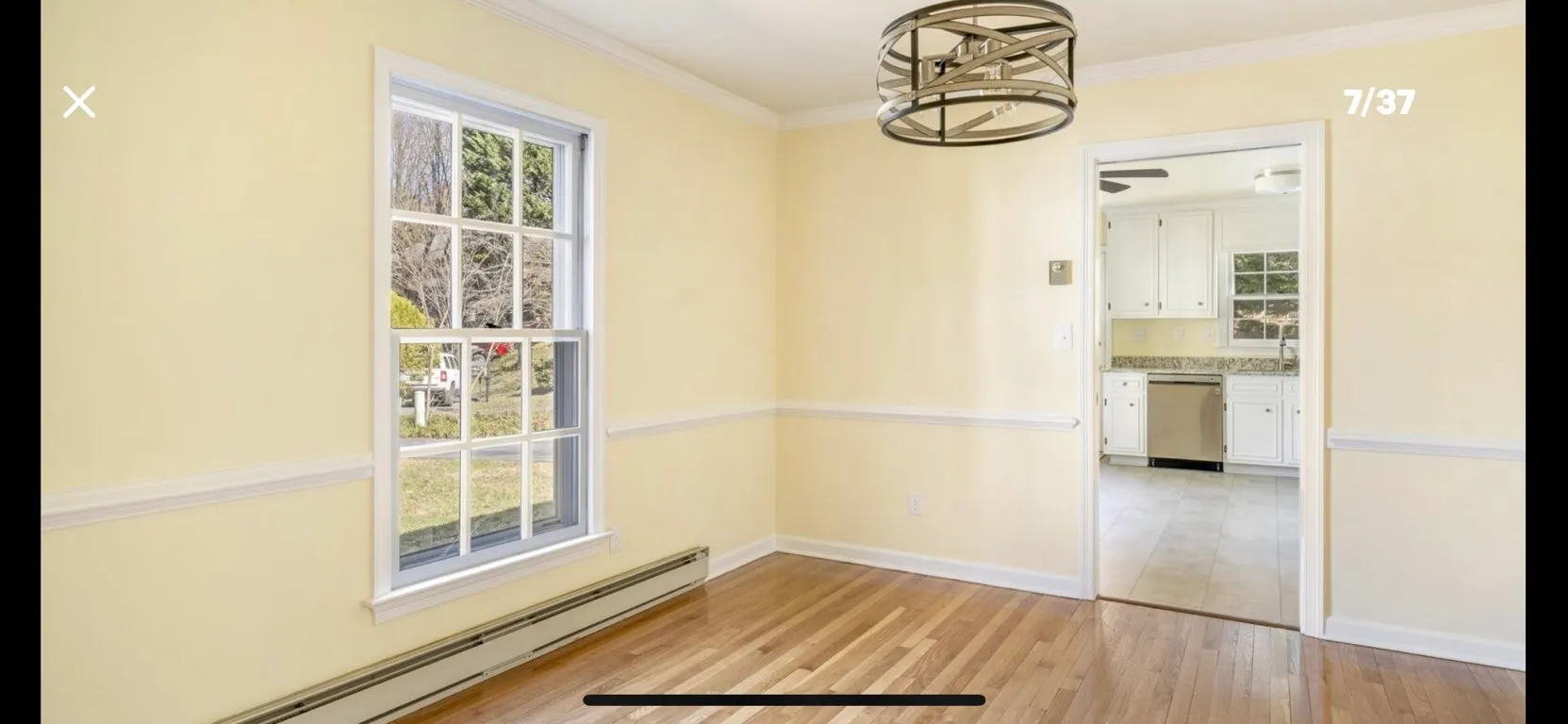 Bright yellow dining room with white wainscoting, hardwood floor, and view into white kitchen