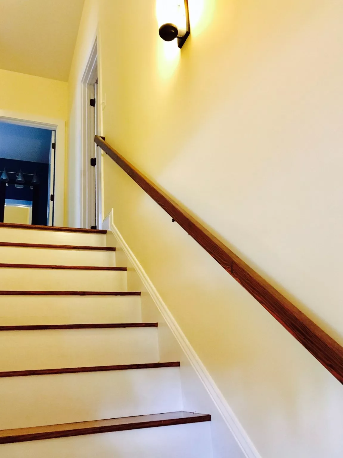 Bright yellow stairwell with wooden handrail and white trim leading upward