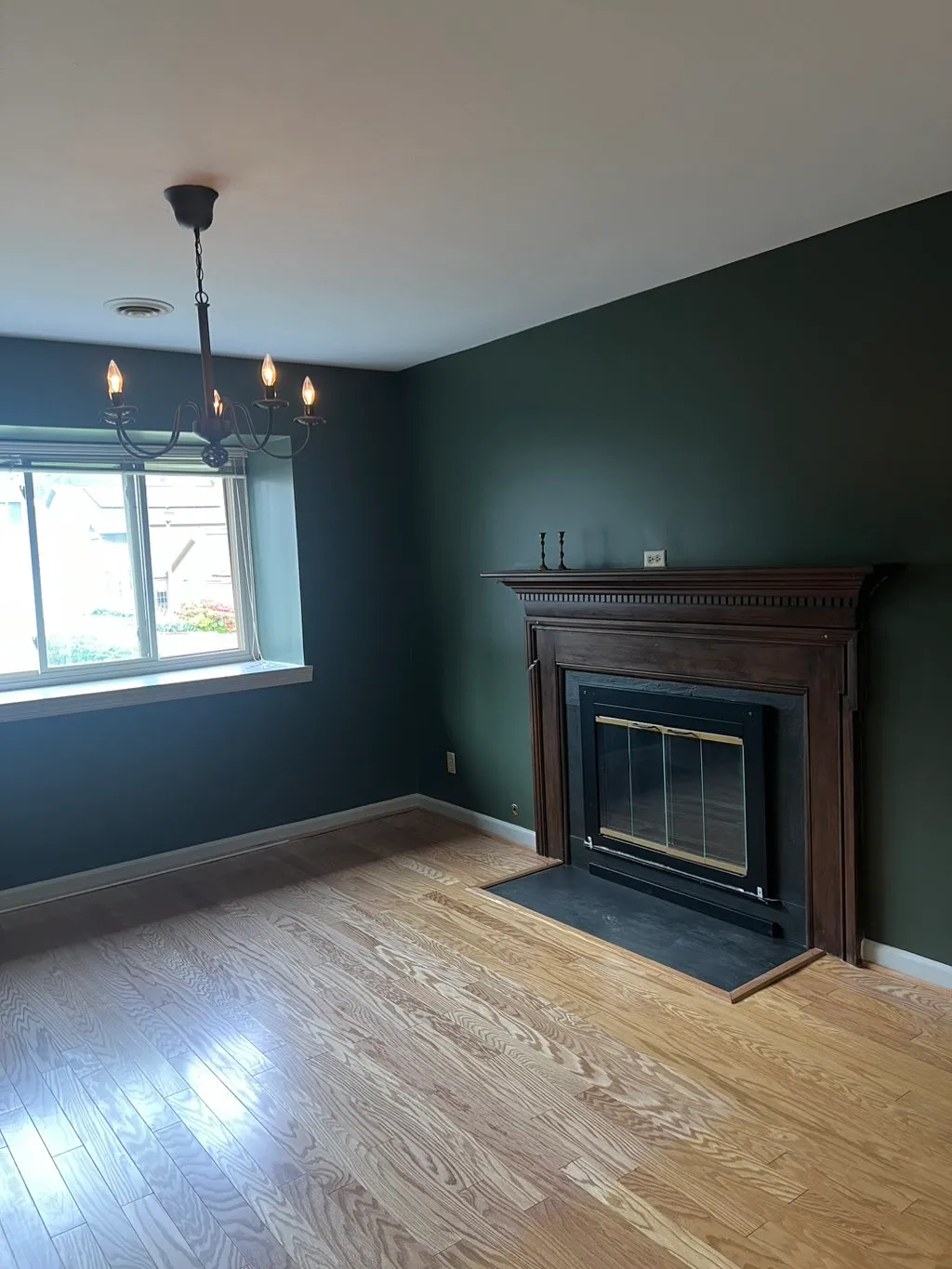 Modern living room with dark green walls, wood fireplace, chandelier, and hardwood flooring