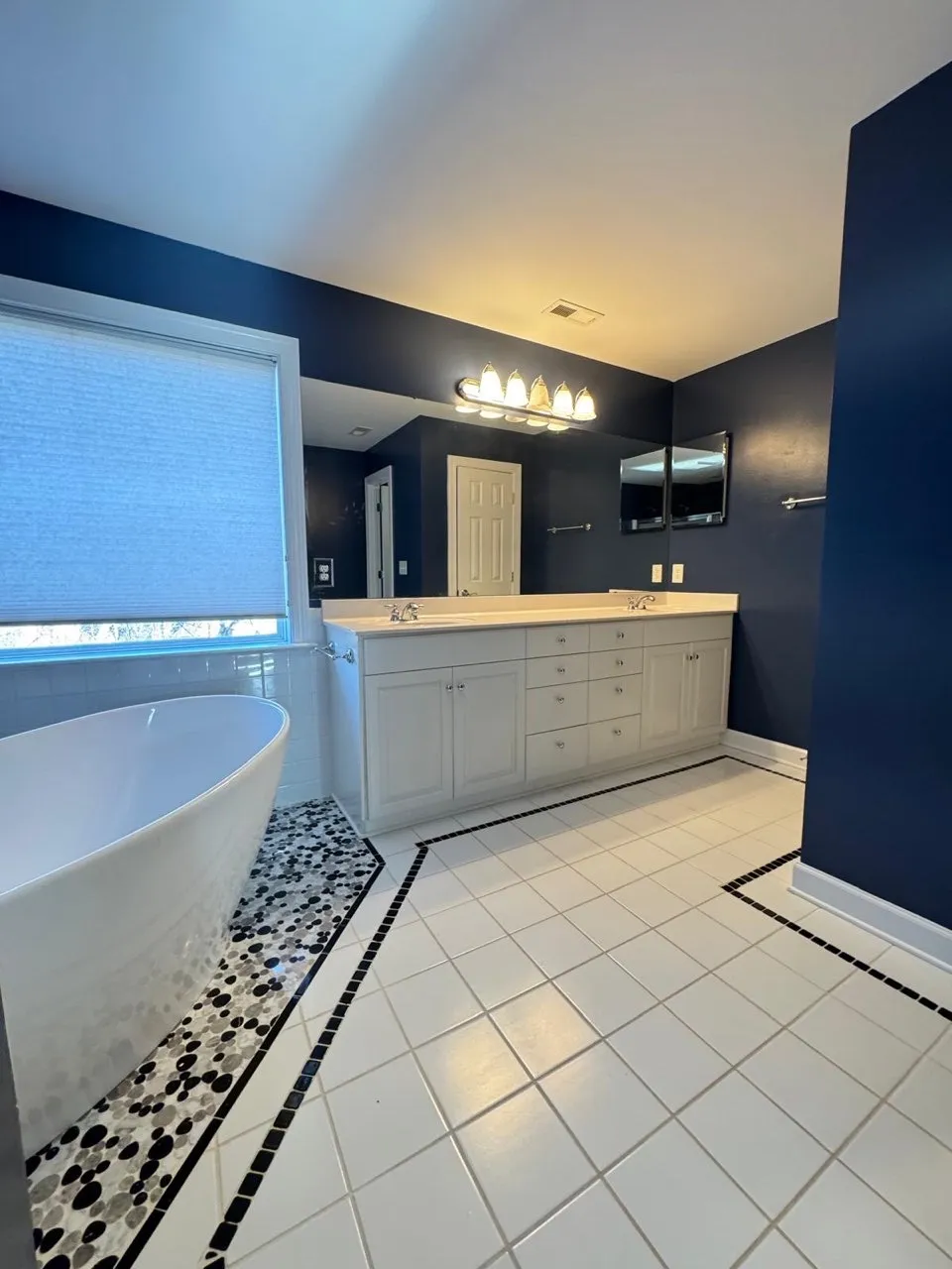 Modern master bathroom with dark blue walls, white vanity cabinet, dual sinks, soaking tub, and decorative tile flooring