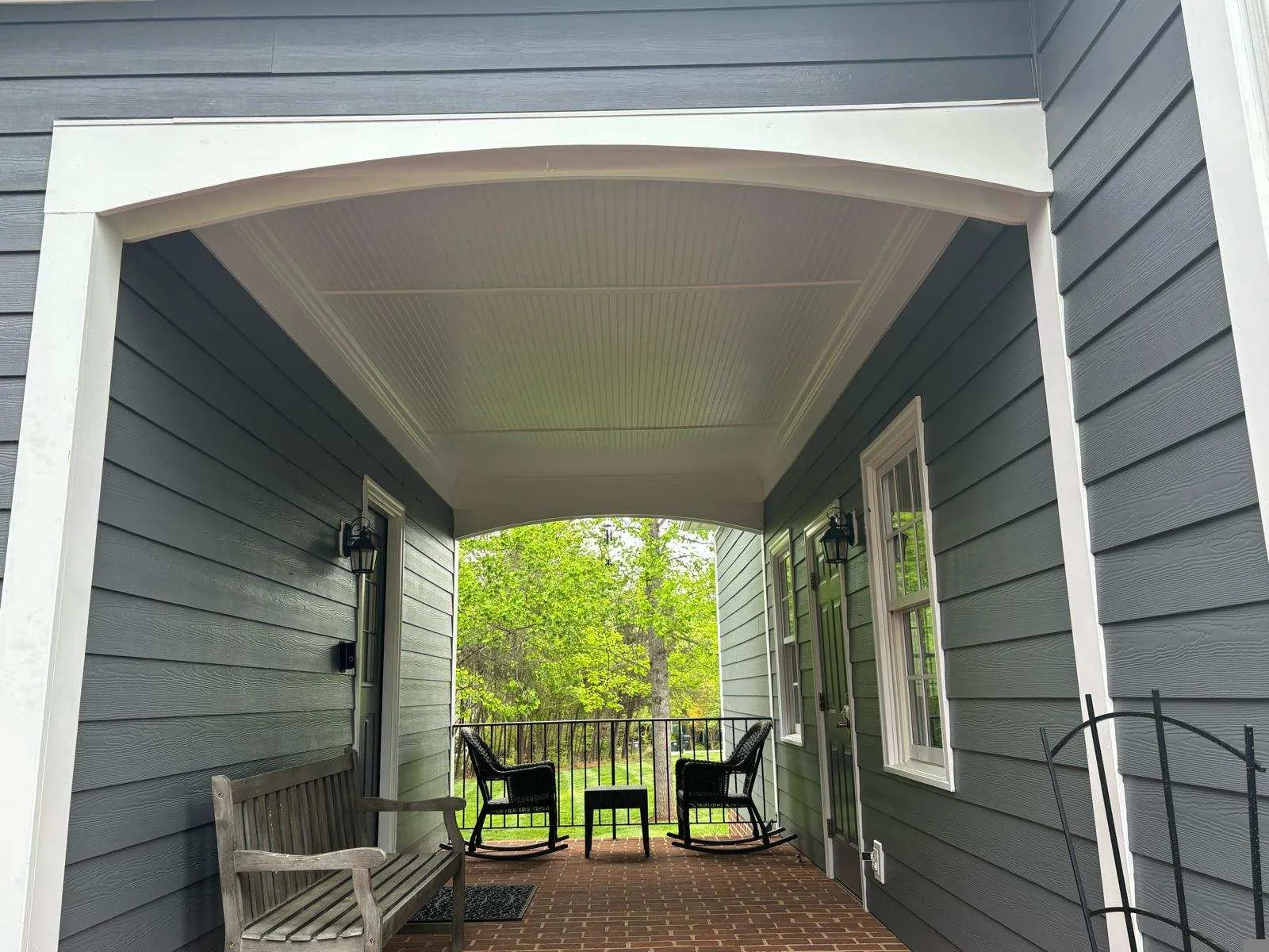 Covered porch with rocking chairs overlooking green trees and railing