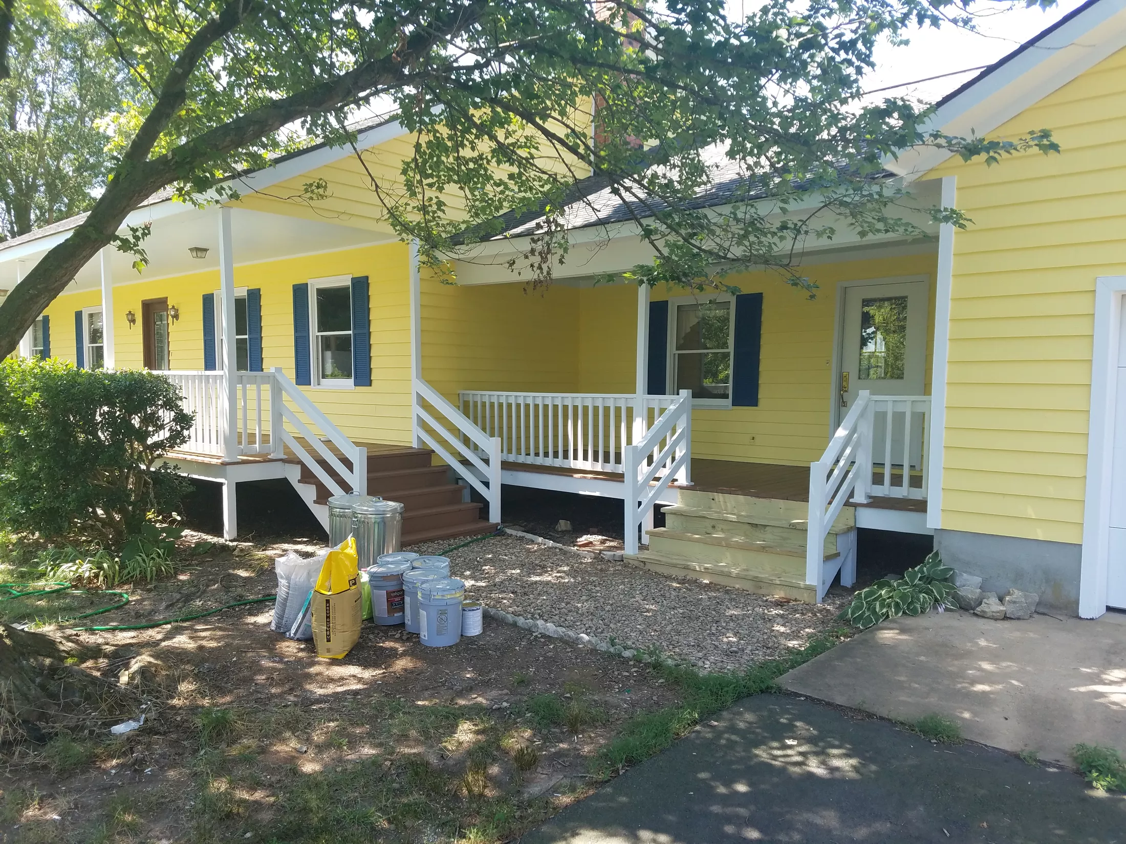 Bright yellow house with white trim, blue shutters, and covered front porches during renovation