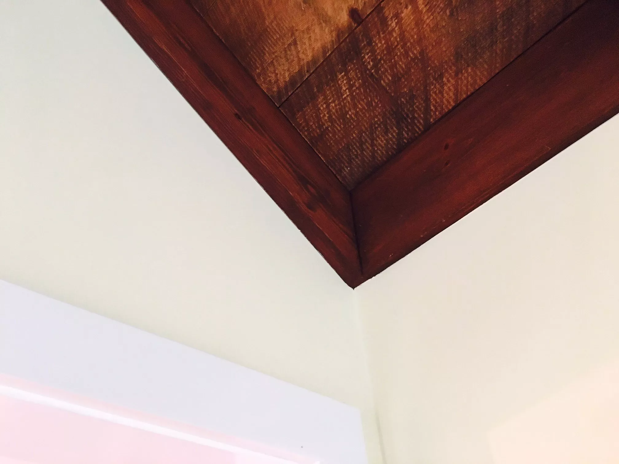 Dark wood ceiling beam against cream-colored ceiling in interior space